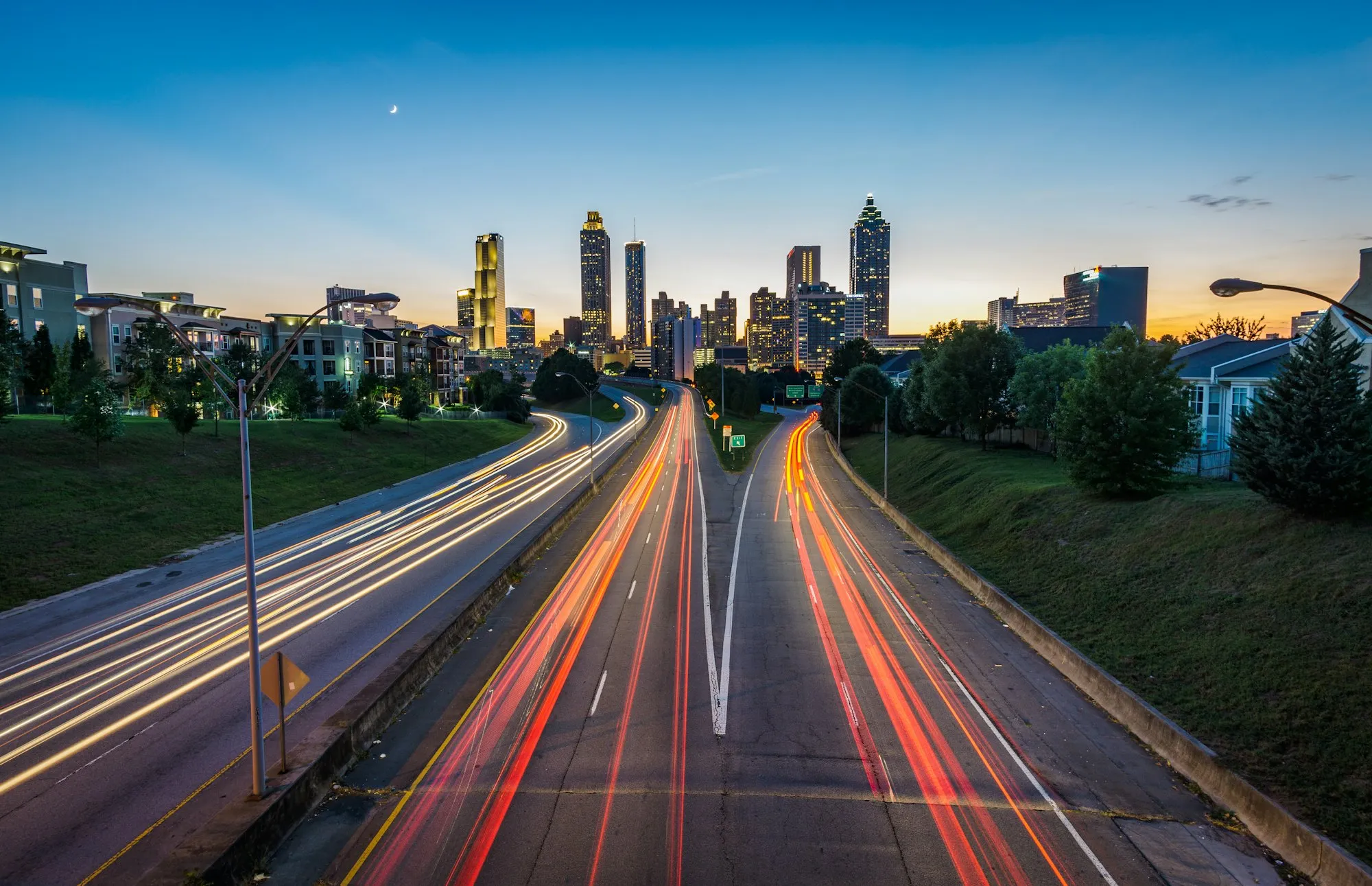 A highway streaked with light trails leading into a city at dusk